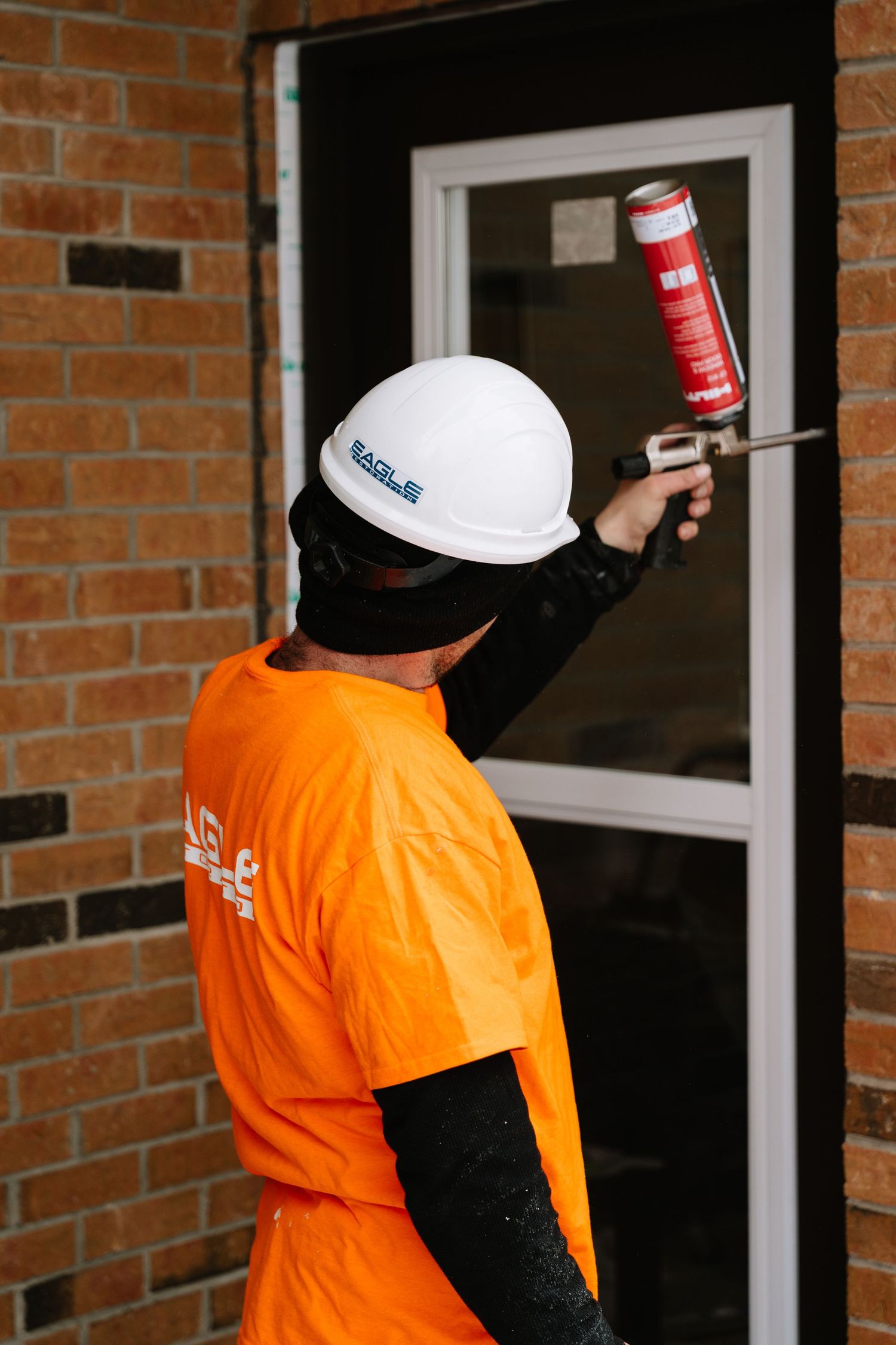 Maintenance crew in orange safety gear working on exterior window installations on a brick wall.