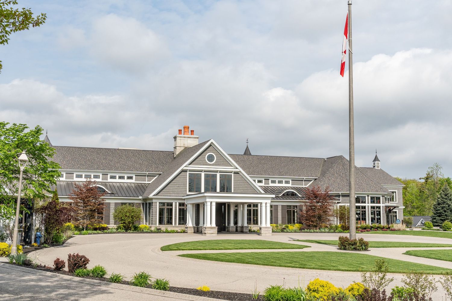 Elegant Canadian country club exterior with circular driveway, manicured gardens, and Canadian flag on tall flagpole.