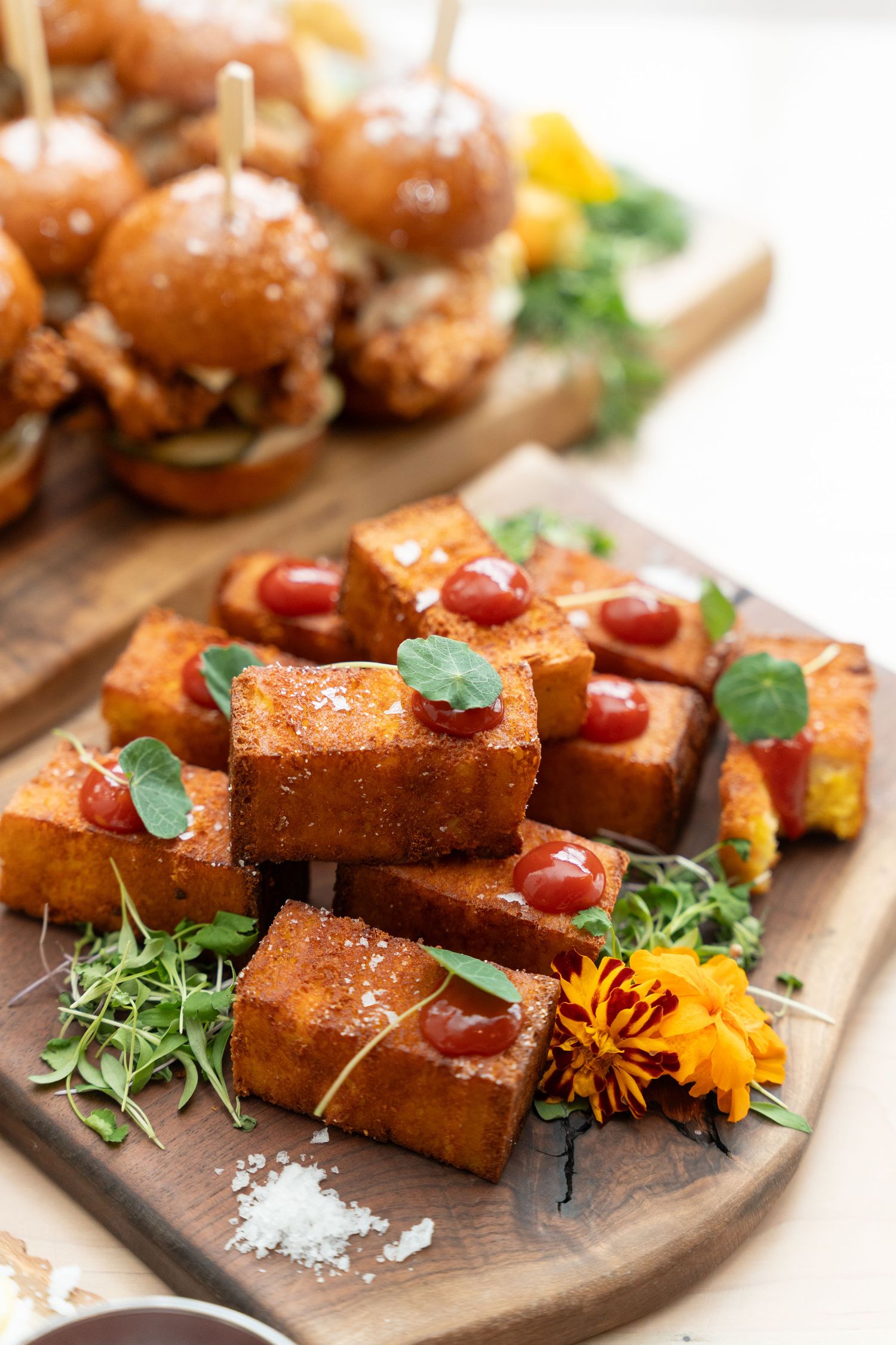 Artistically plated appetizers on dark slate board with edible flowers and microgreens.