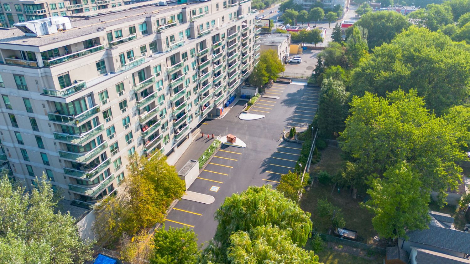 Aerial view of modern apartment building with white facade and balconies next to green park area and parking lot.