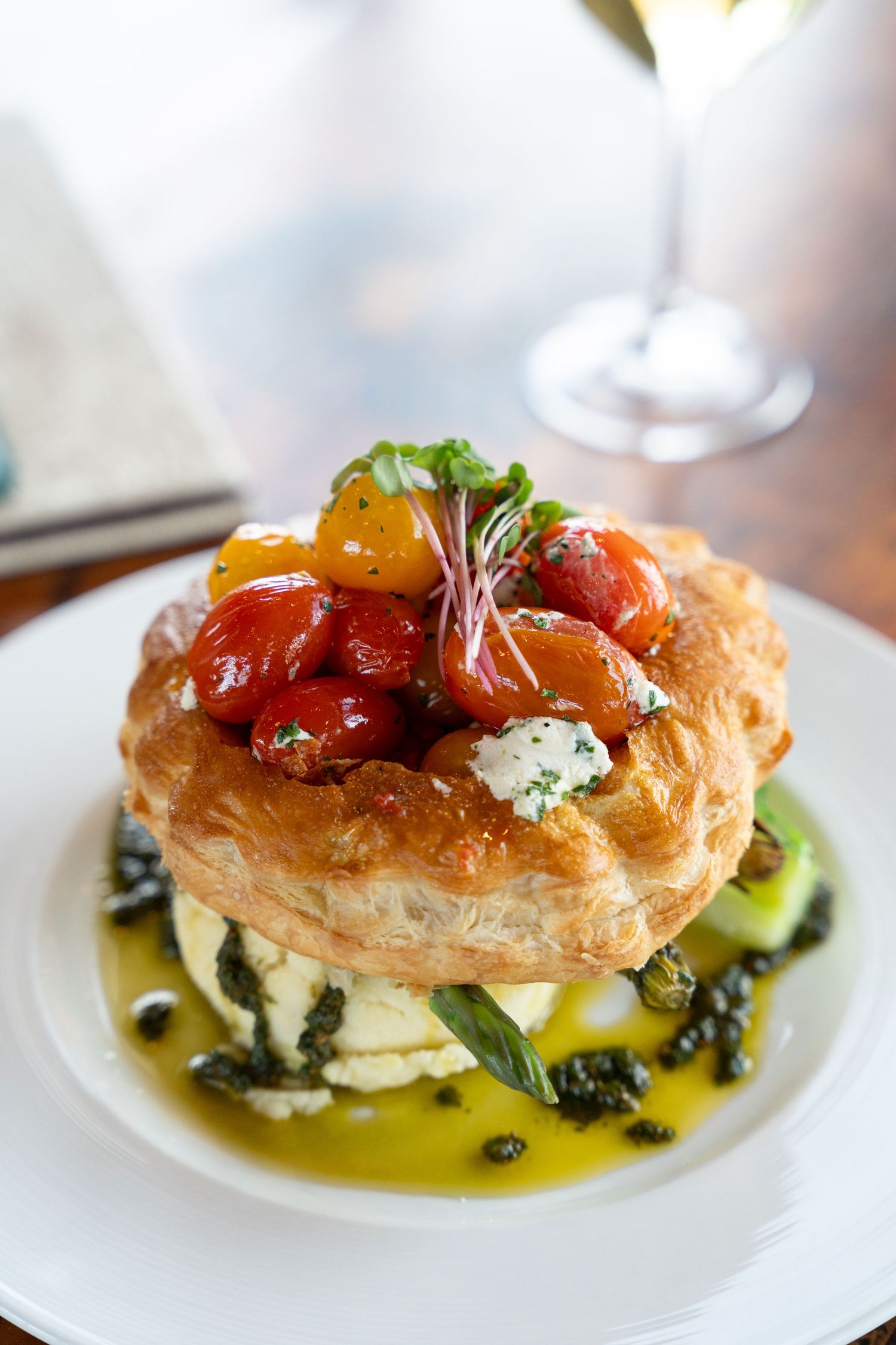 Elegant plated appetizer featuring golden puff pastry topped with roasted tomatoes and fresh herbs in olive oil.
