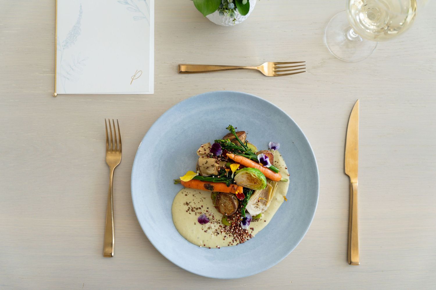 Elegant plated dish with golden brown meat and colorful garnishes served on a light blue ceramic plate with gold cutlery.