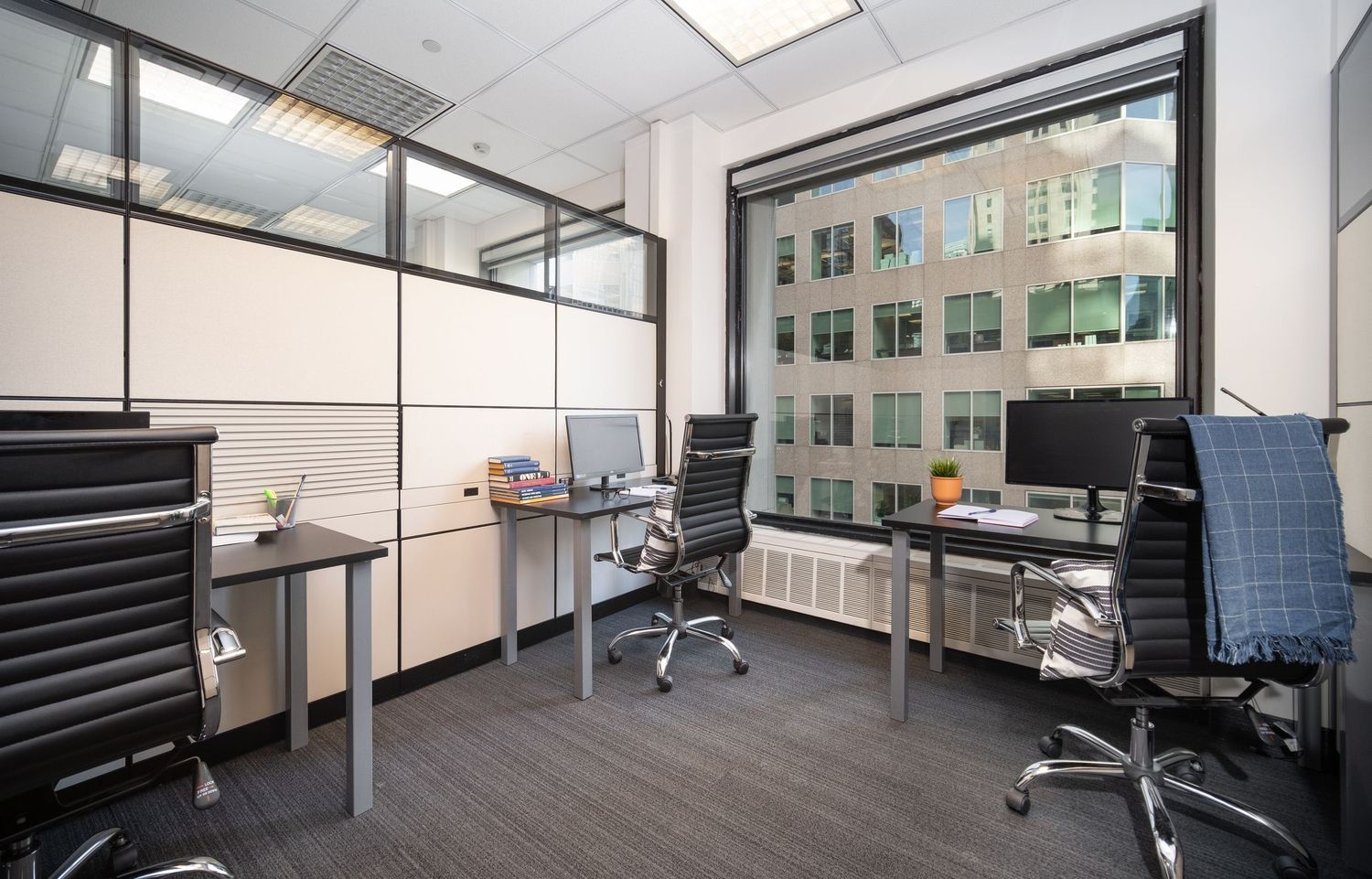 Open concept office space with white walls, desks, and large windows providing natural light.