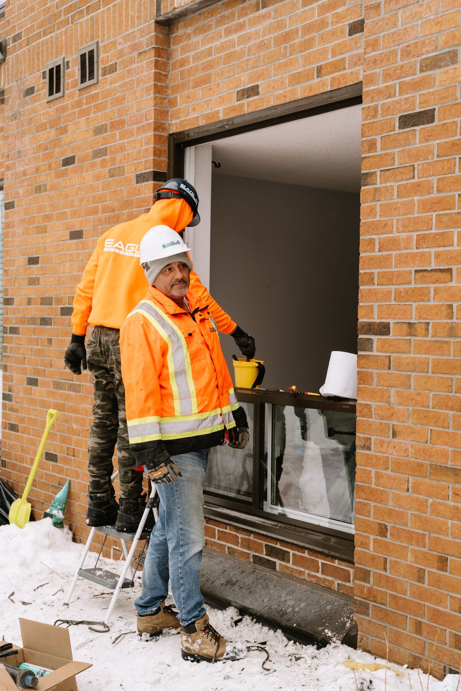 Maintenance crew in orange safety vests work on exterior windows of a residential building.