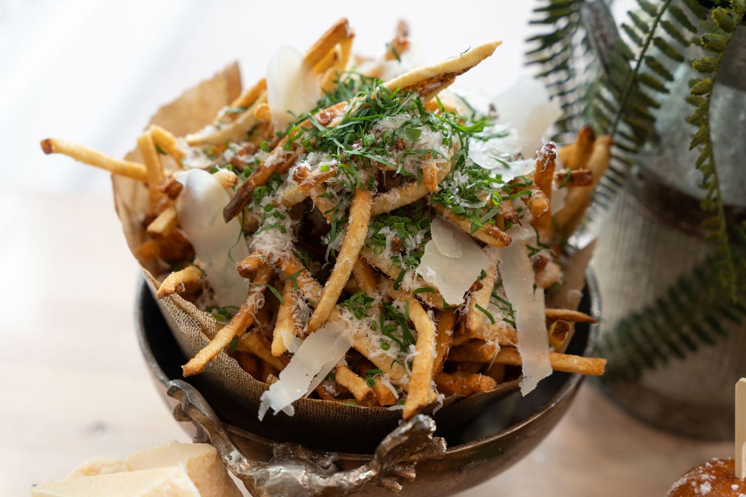 Crispy french fries topped with fresh herbs and shaved parmesan cheese served in a rustic bowl.