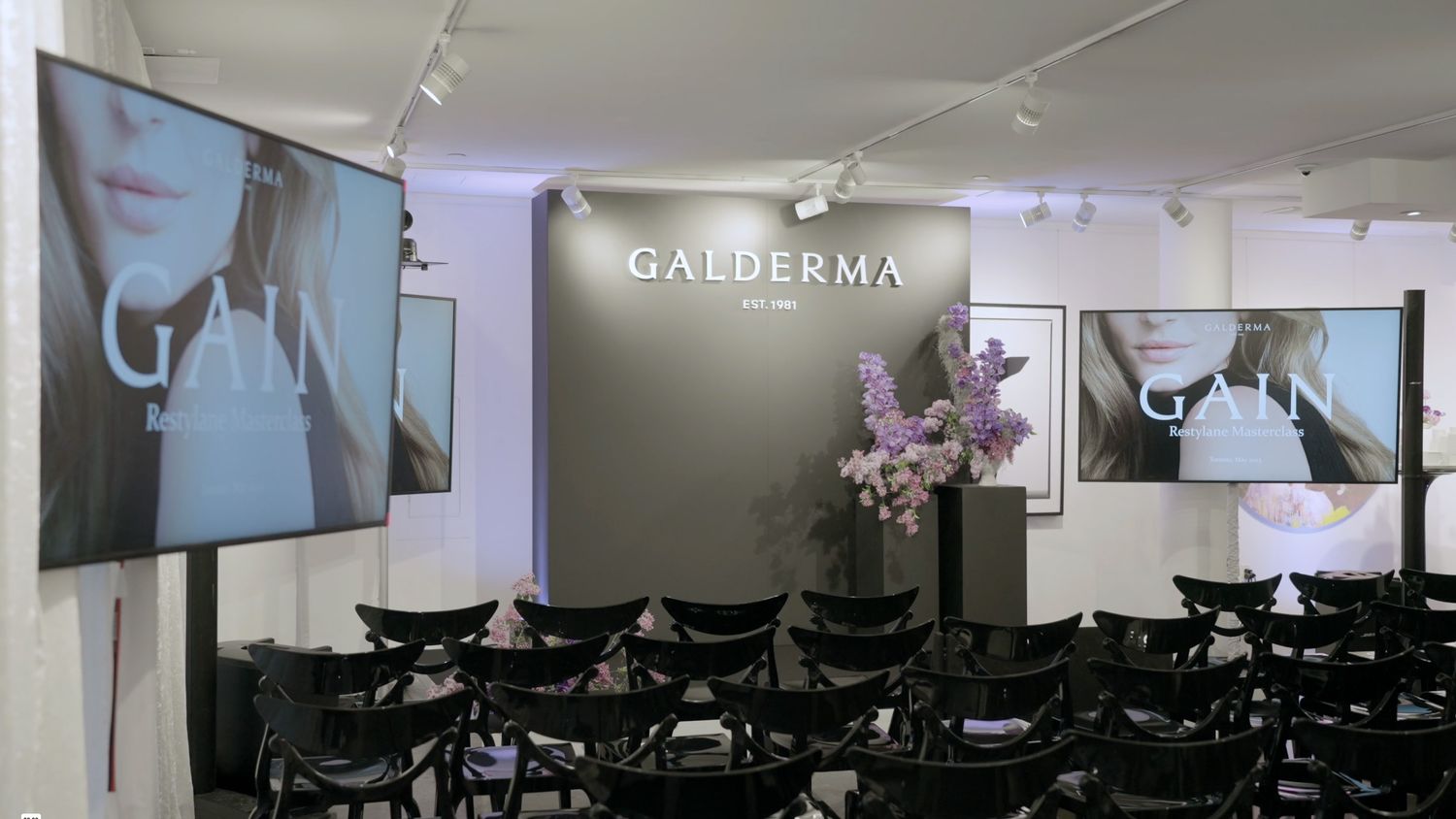 Modern conference room with rows of black chairs facing a projector screen and presentation setup.