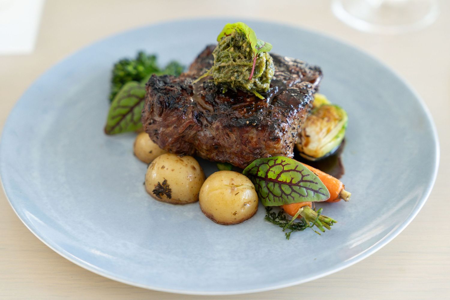 A series of plated dishes featuring grilled meats with roasted potatoes and fresh vegetables on light blue plates.