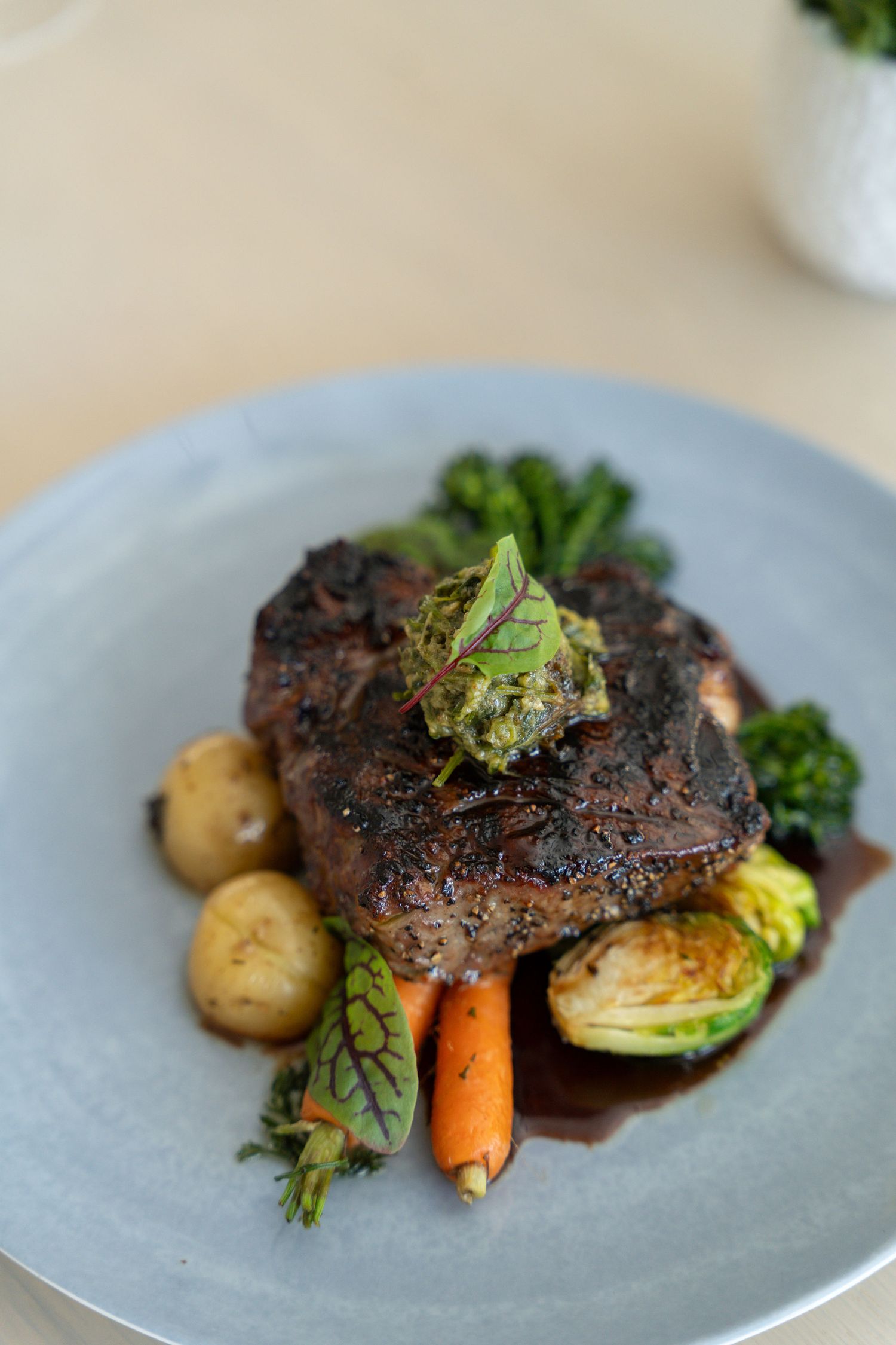 Grilled steak with roasted vegetables and potatoes served on a gray plate with elegant plating.