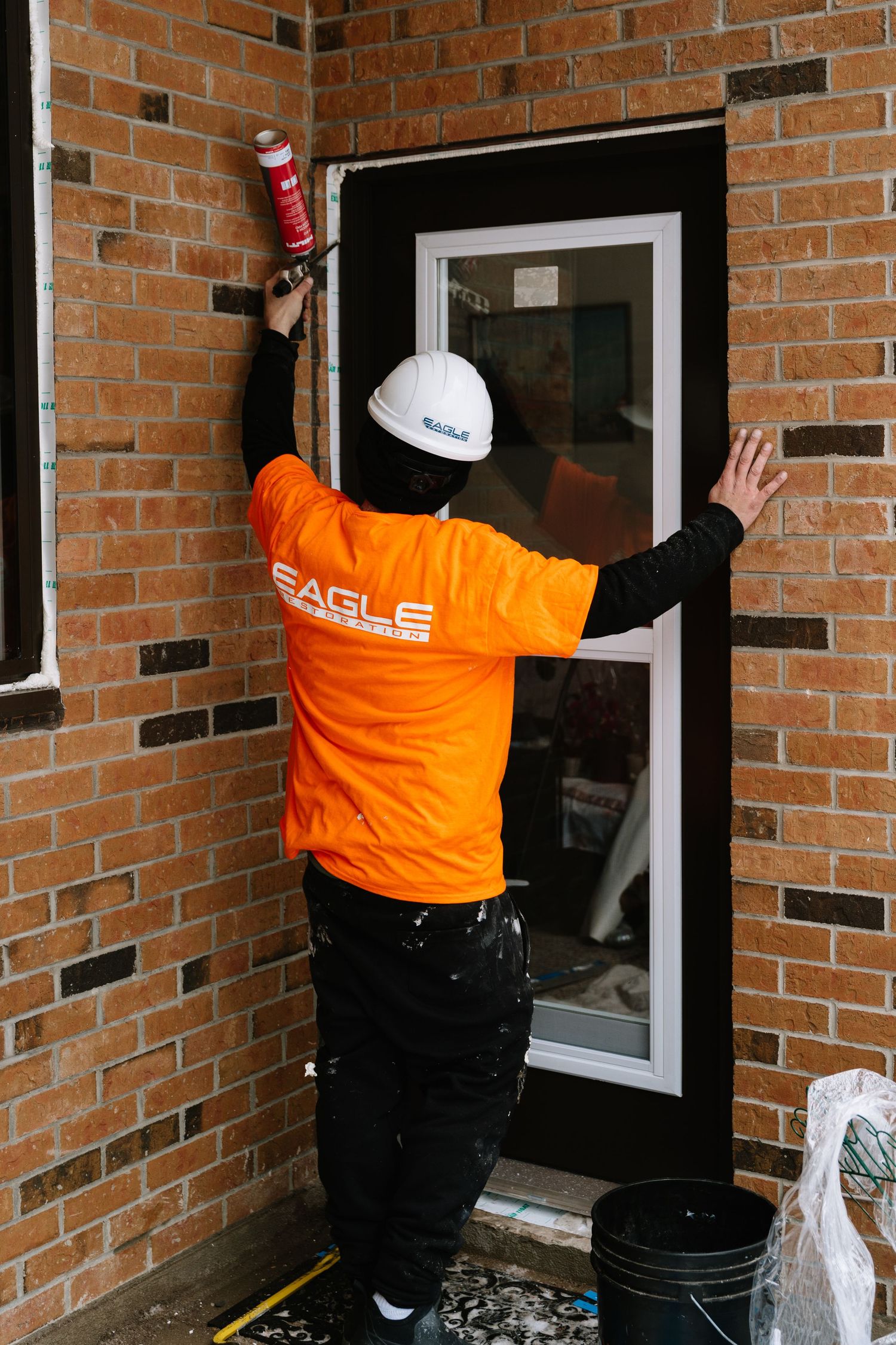 Workers in bright orange uniforms clean multiple windows on a brick apartment building.