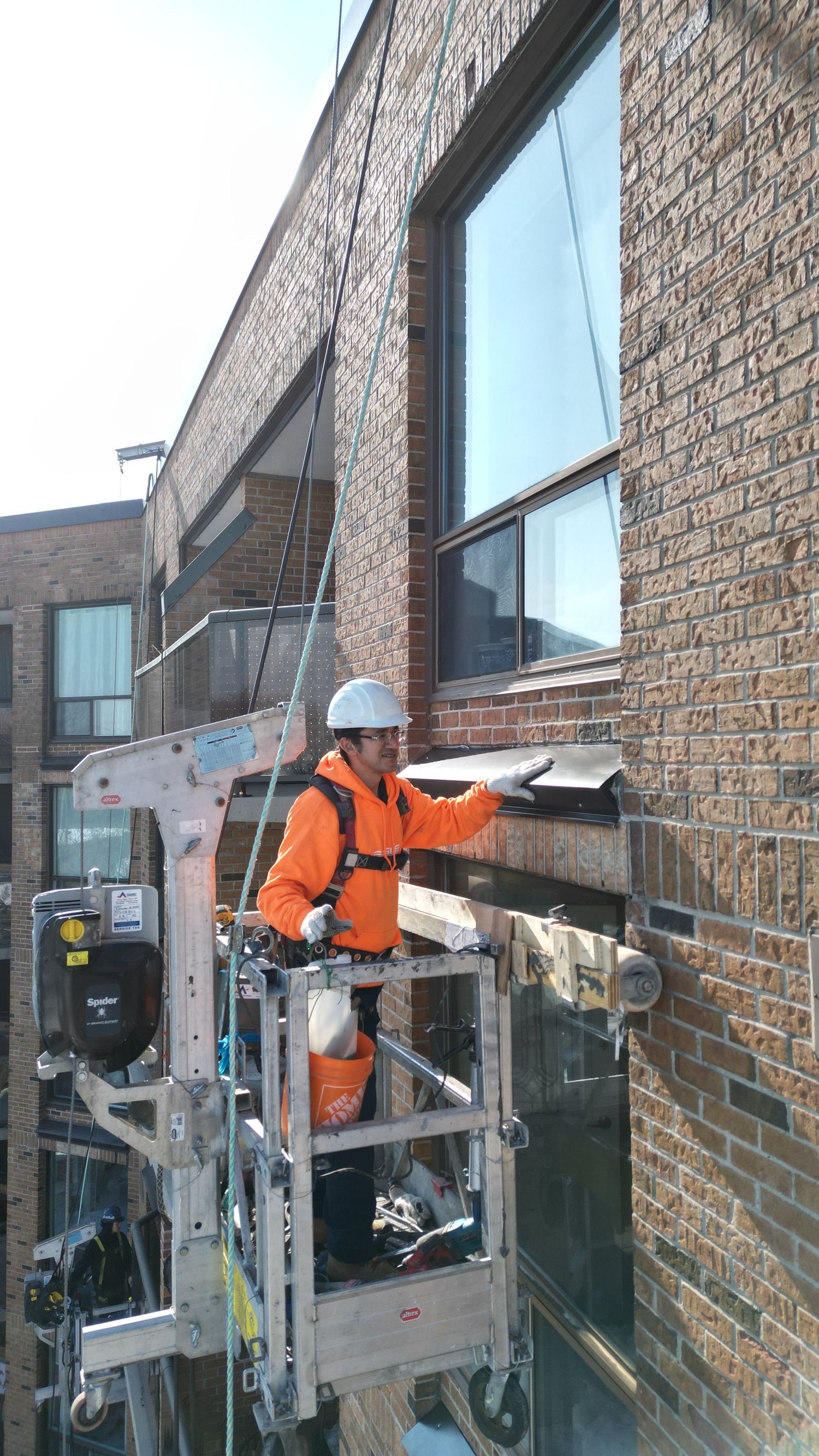 Professional window cleaner in safety harness working on exterior building maintenance with cleaning equipment.