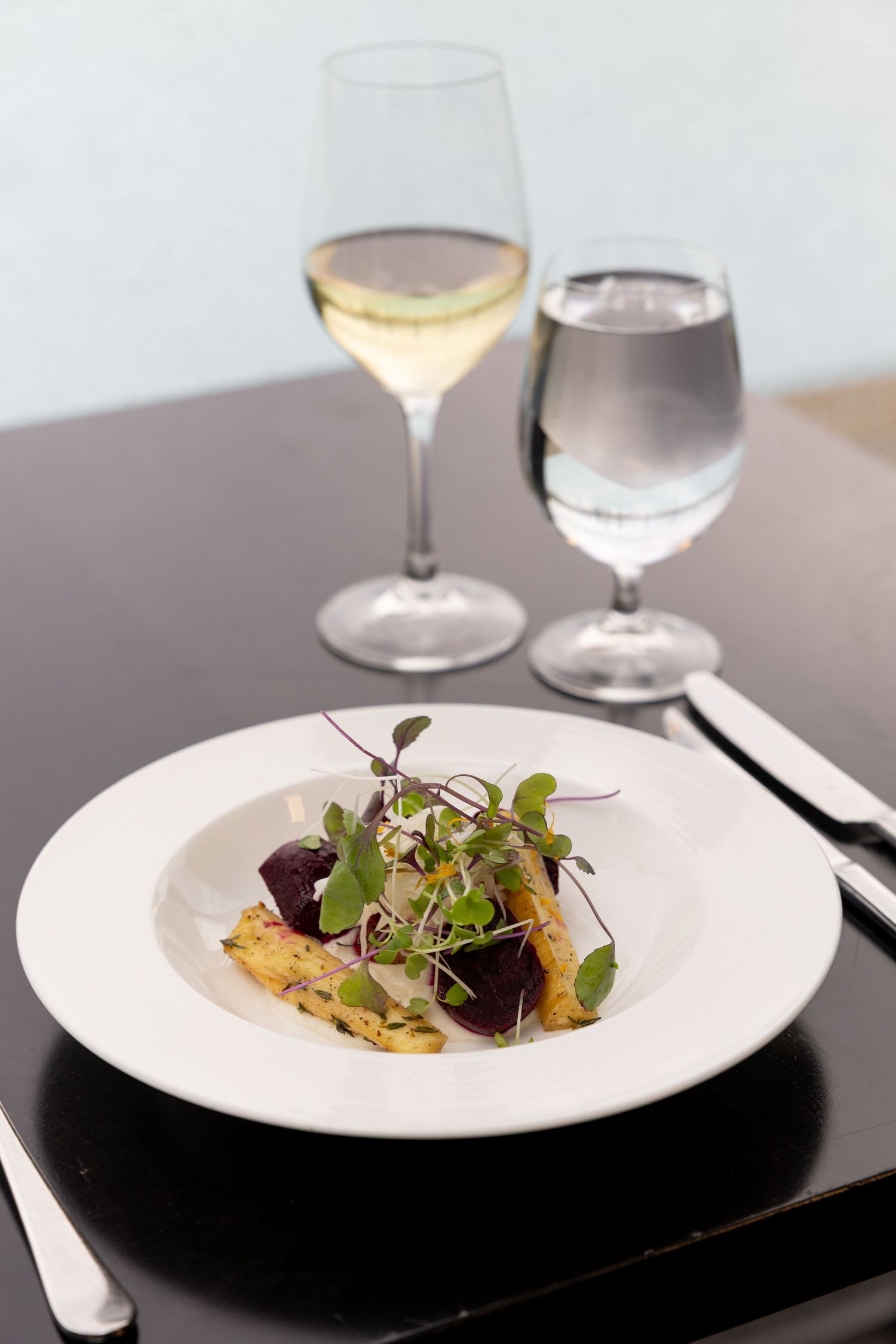 A sequence of four elegant plated dishes with microgreens and garnishes served on white plates against a dark surface.