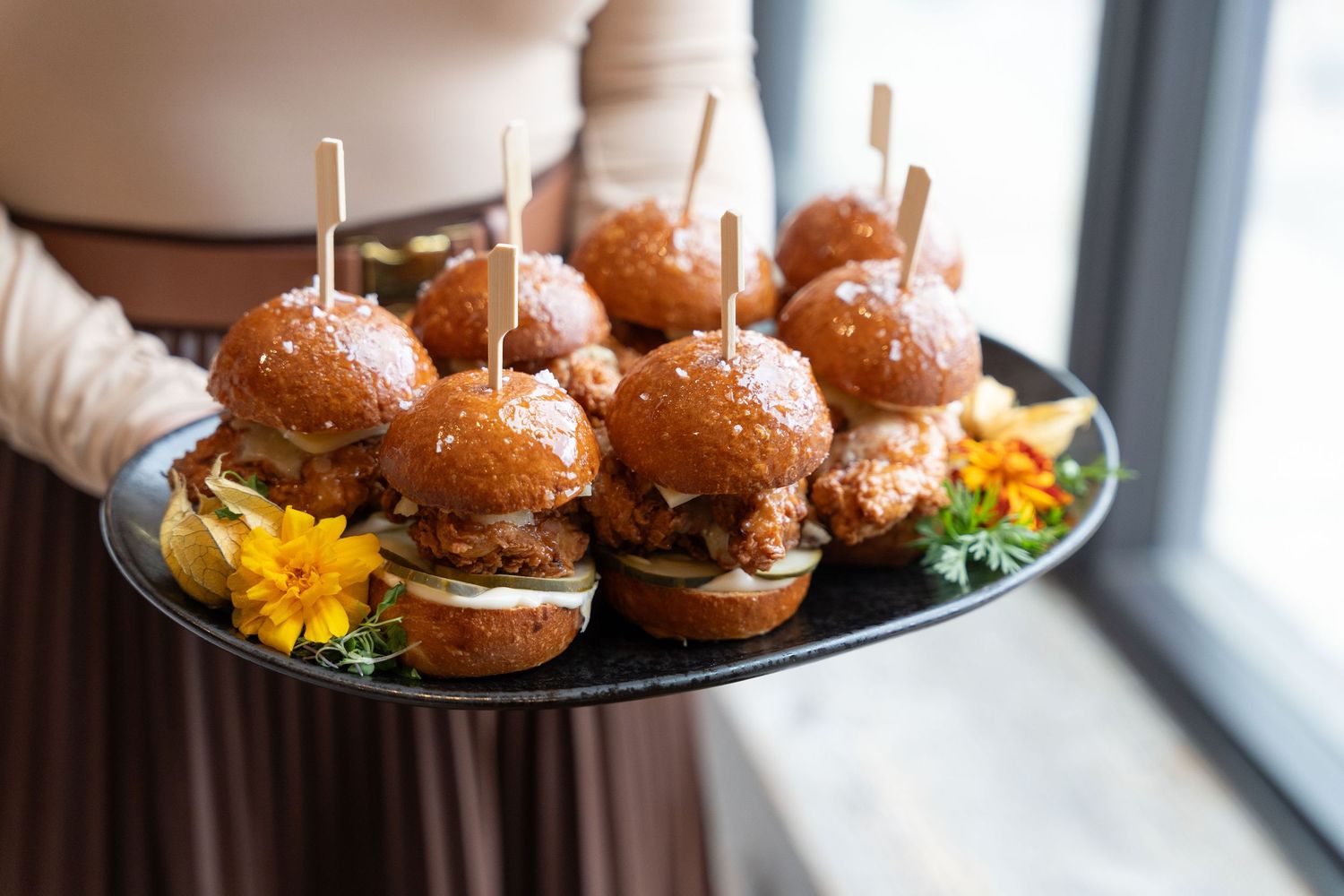 Gourmet sliders with brioche buns arranged on a black serving platter near a bright window.