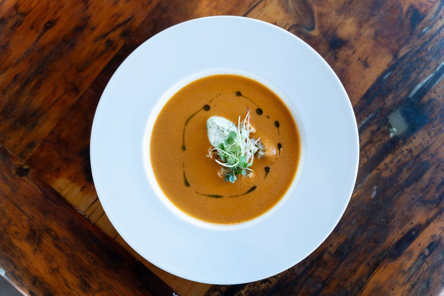 Five bowls of creamy pumpkin soup garnished with fresh herbs on a rustic wooden table.