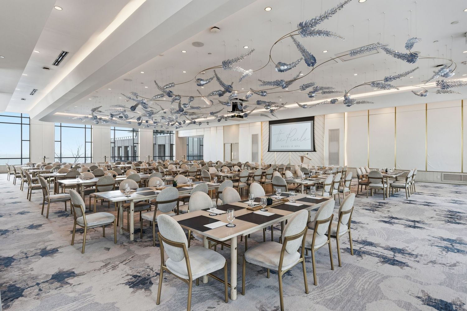 Modern corporate training room with white tables and chairs arranged in rows on a blue patterned carpet.