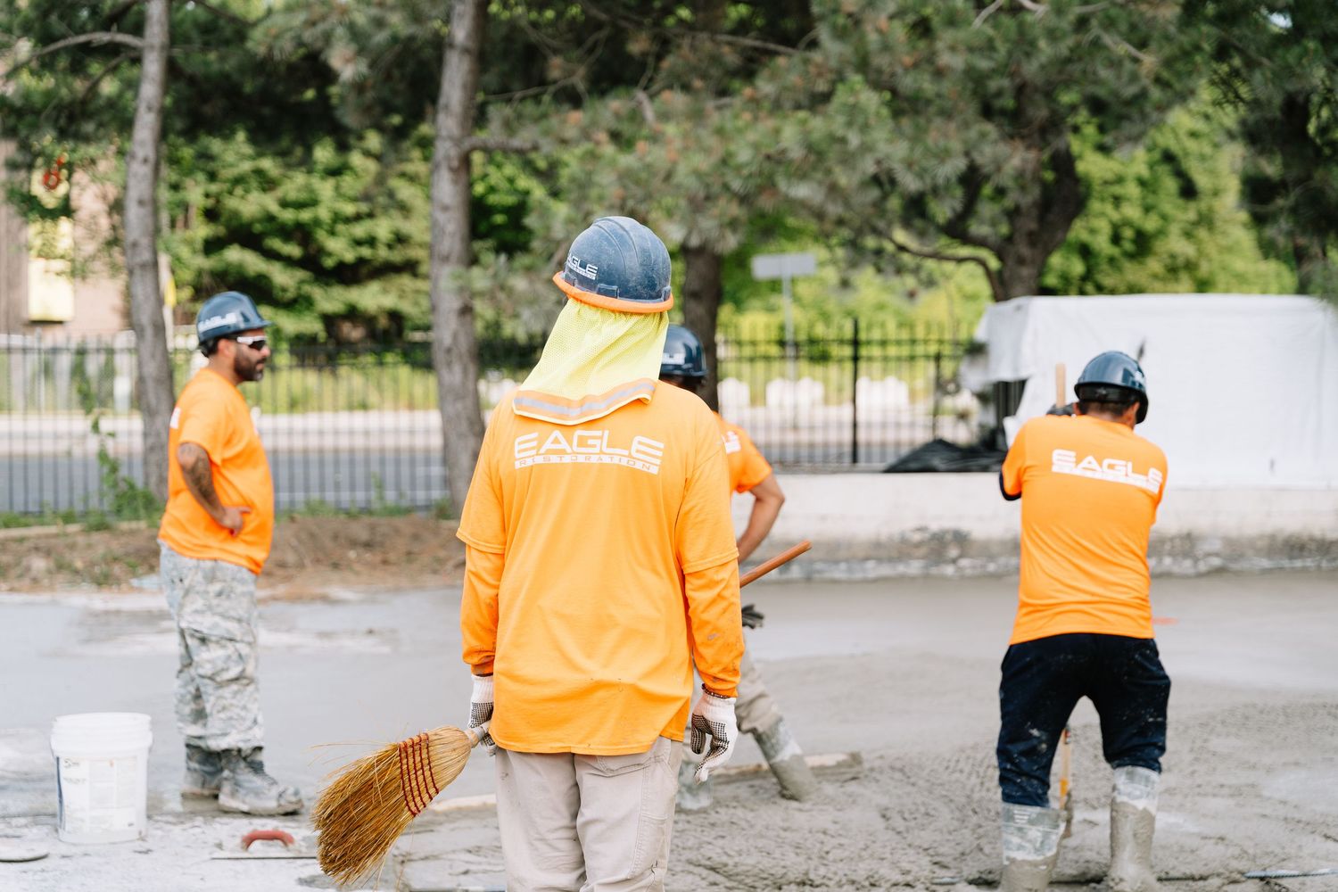 Workers in orange safety vests performing construction tasks at an outdoor worksite.