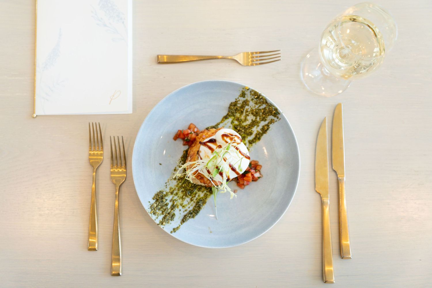 Fine dining table setting with seafood and asparagus dishes on pale blue plates accompanied by golden utensils.