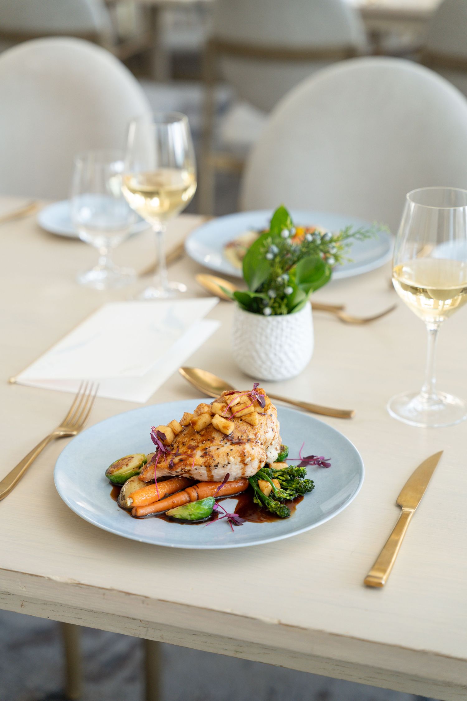 Beautifully plated salmon dish with roasted vegetables served on light blue plate with wine pairing.