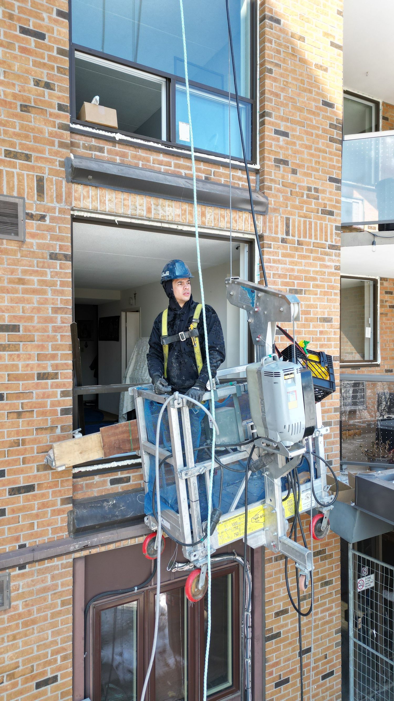 Window cleaners on suspended platforms service the exterior of a brick building.