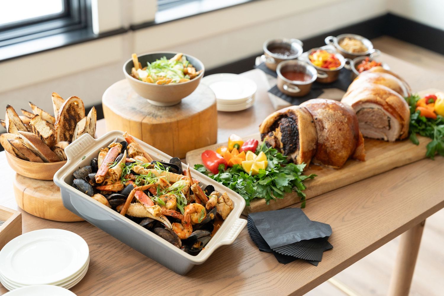 A wooden serving board displays assorted dishes including bread, salads, and appetizers in a bright restaurant setting.