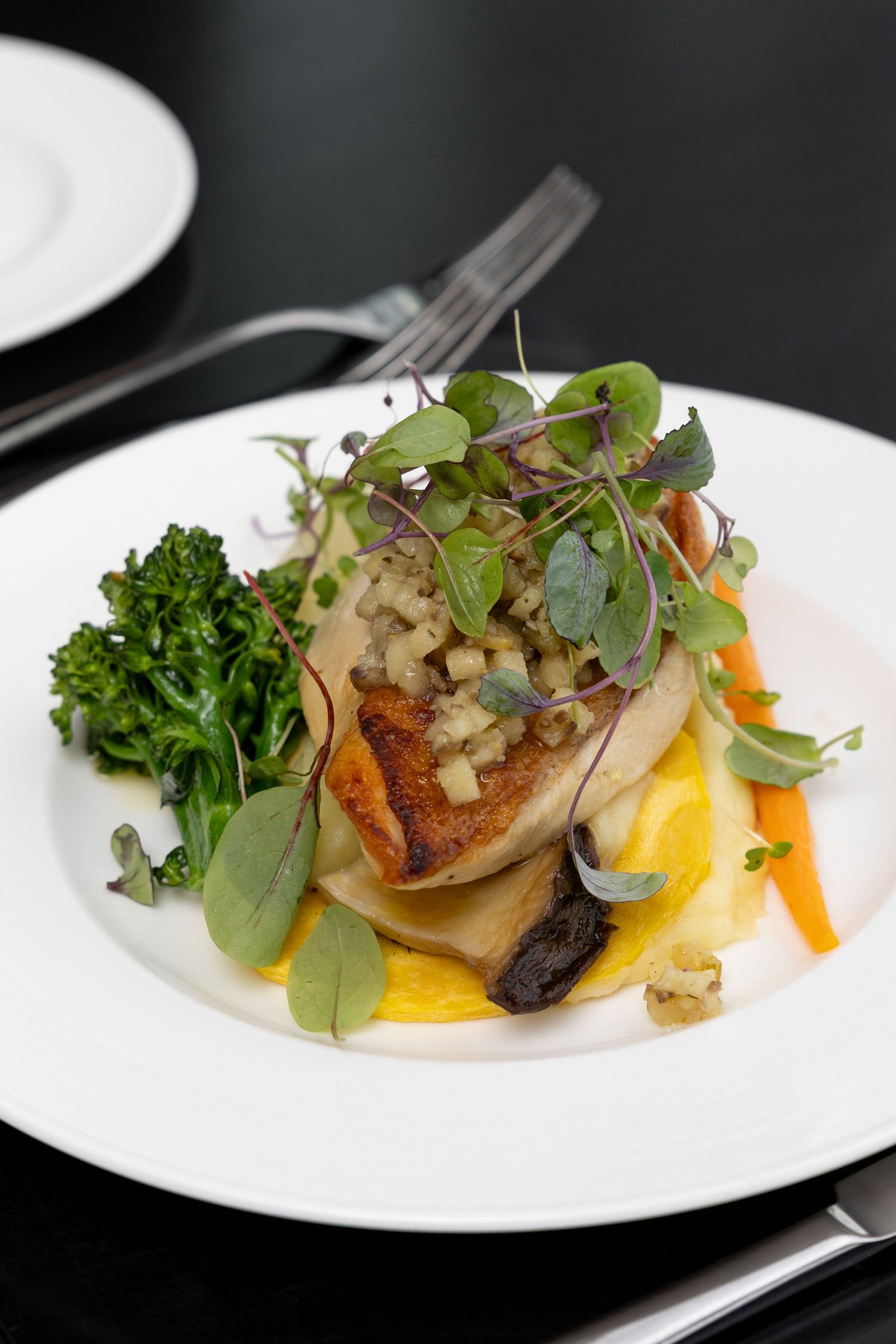 Pan-seared fish fillet with colorful vegetables and microgreens plated elegantly on white dinnerware.