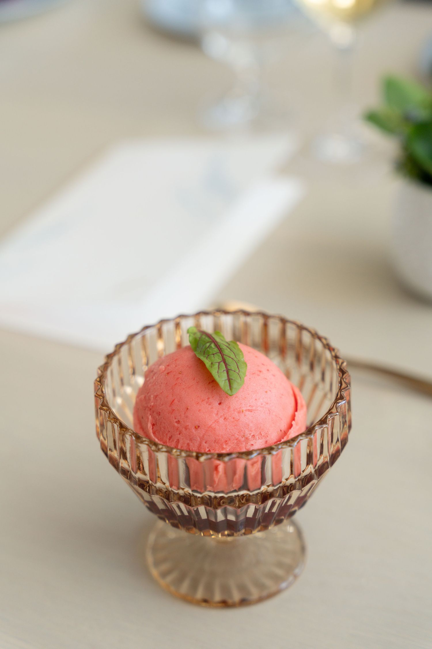 Pink sorbet or ice cream scoop garnished with mint leaf served in a vintage-style ribbed glass dessert bowl.