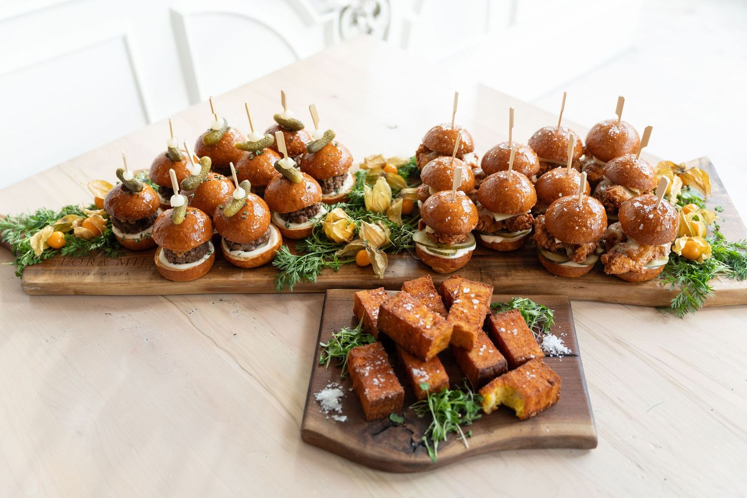 Long wooden serving board filled with rows of mini sliders and appetizers.