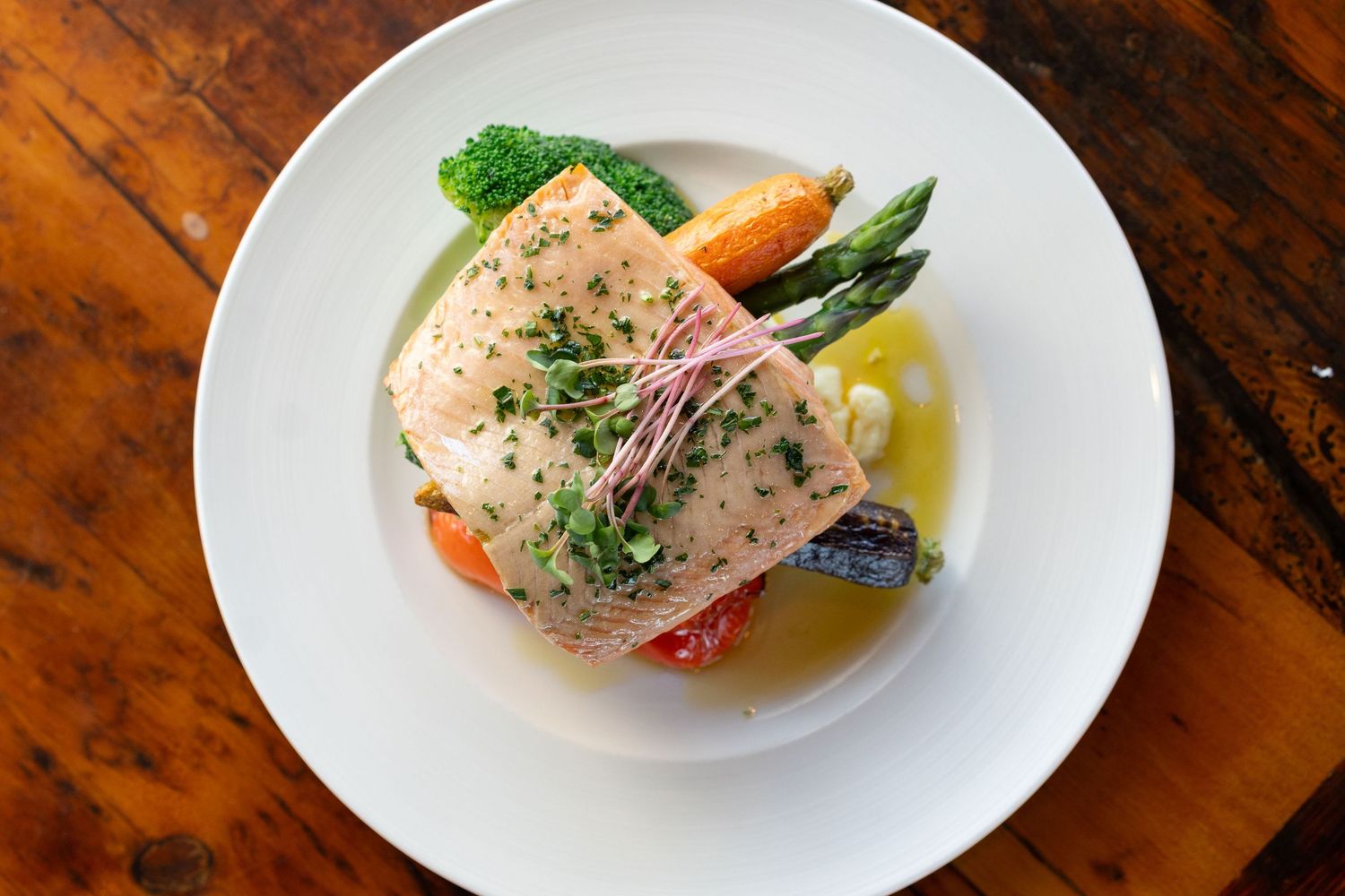 Elegant plated seafood dishes with colorful vegetables and garnishes served on white plates against a rustic wooden surface.