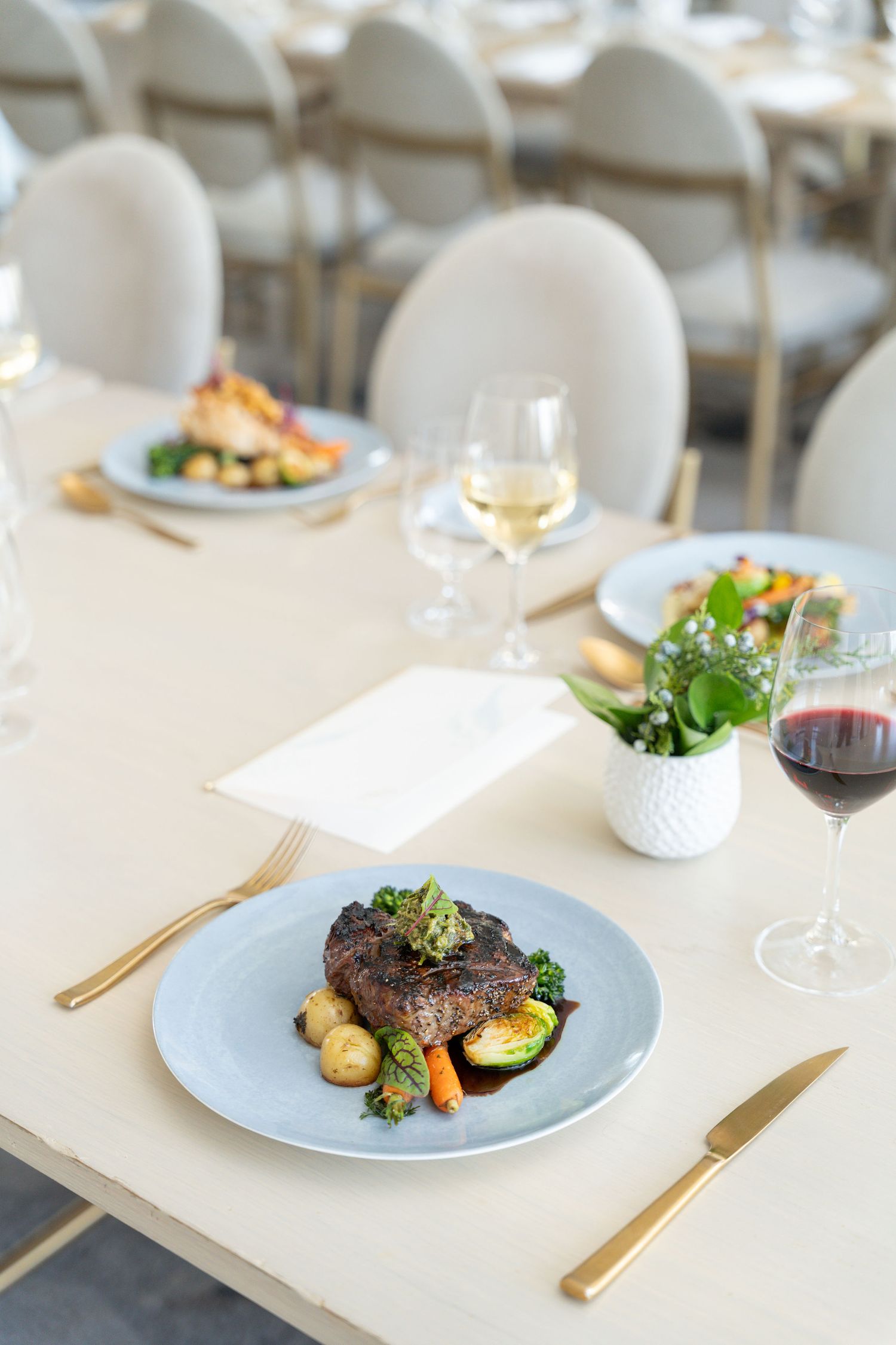 Fine dining table setting with steak dish, wine glasses, and white chairs in an upscale restaurant.