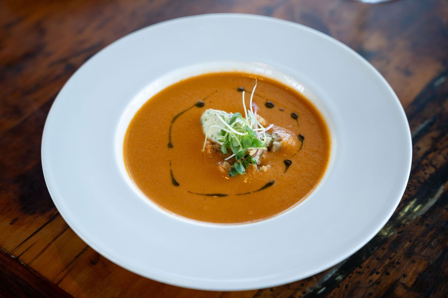 A bowl of creamy butternut squash soup garnished with fresh herbs on a rustic wooden table.