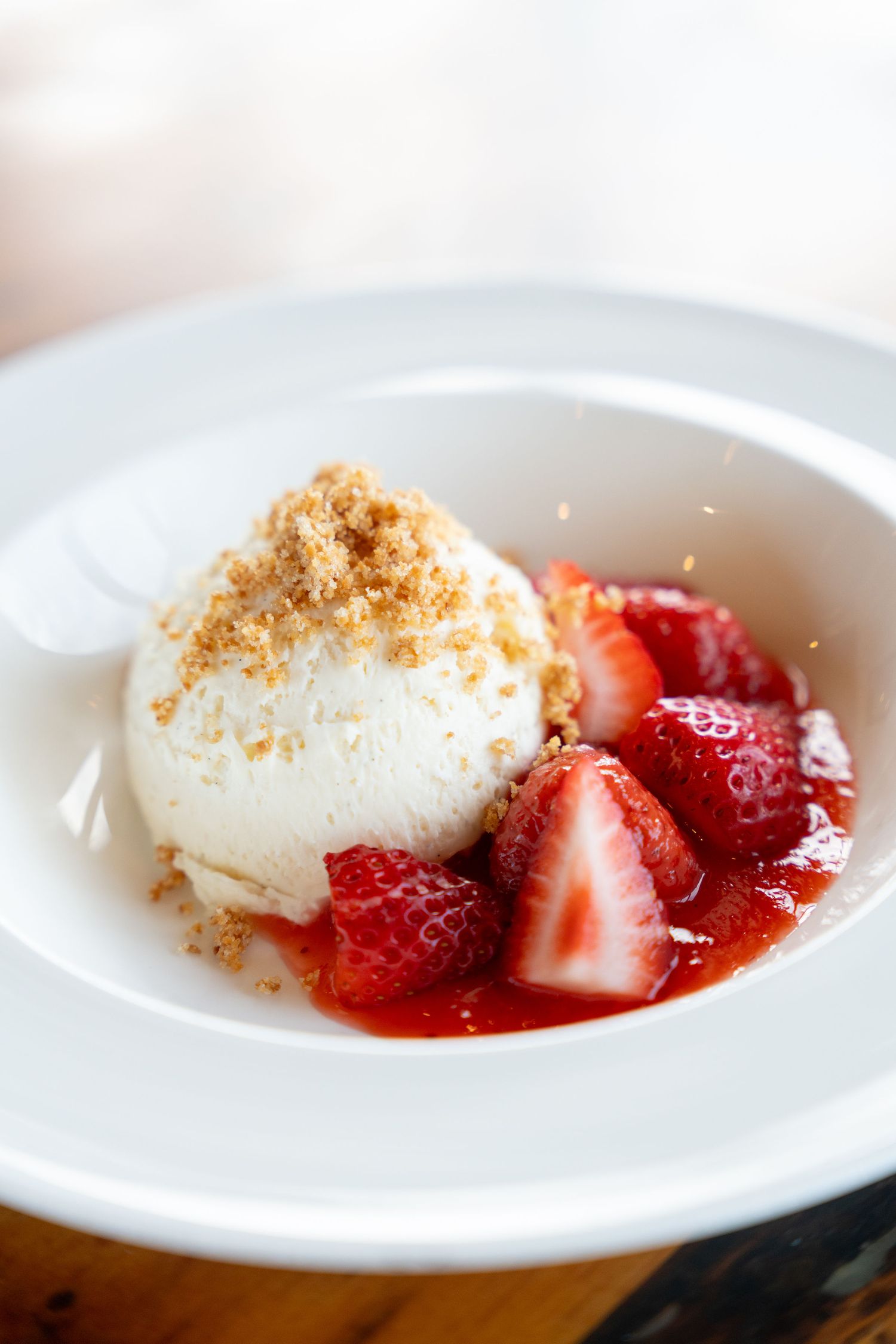 Fresh dessert plate with creamy panna cotta topped with sliced strawberries and crumble garnish.
