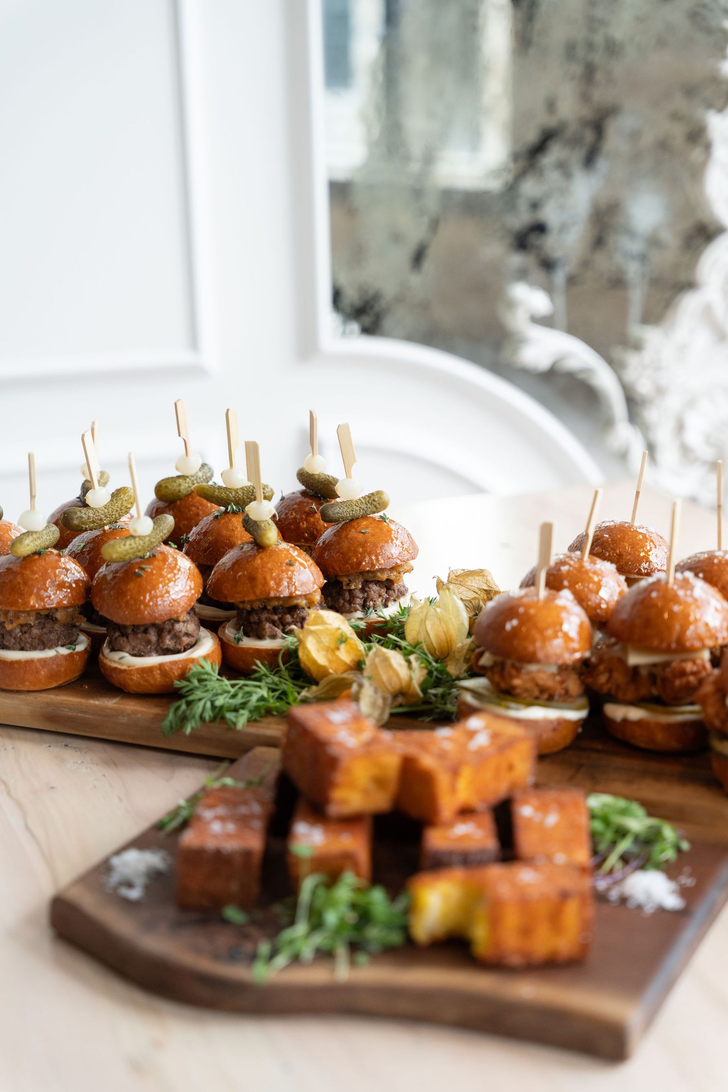 Wooden serving board with rows of gourmet mini sliders garnished with fresh herbs and microgreens.