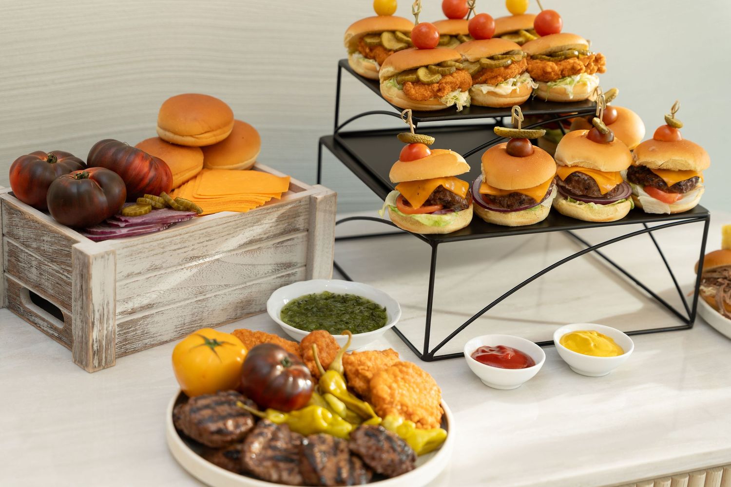 Catering display of gourmet sliders and appetizers arranged on modern black tiered serving stands.