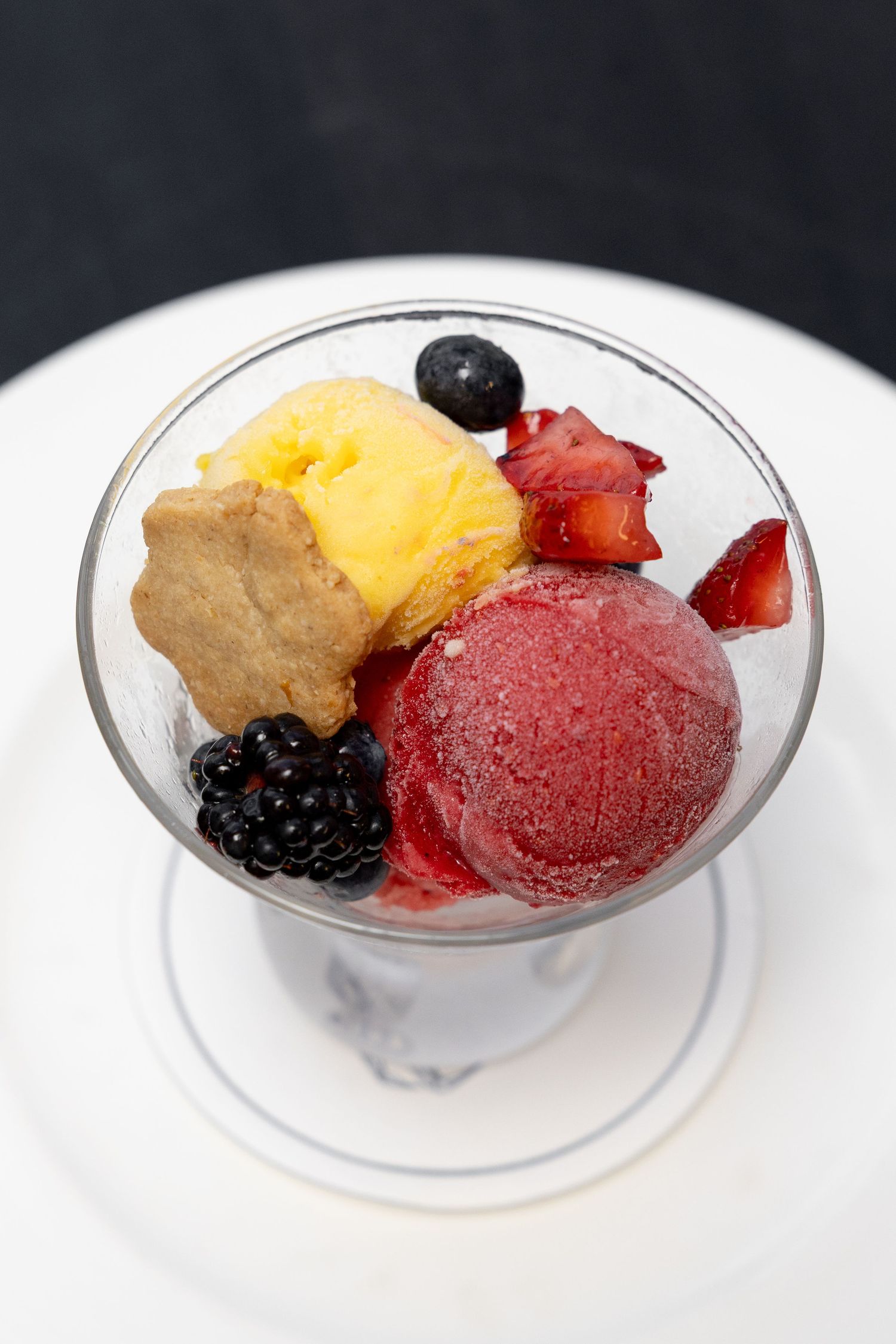 Colorful dessert bowl featuring scoops of fruit sorbet, fresh berries, and cookie garnish.