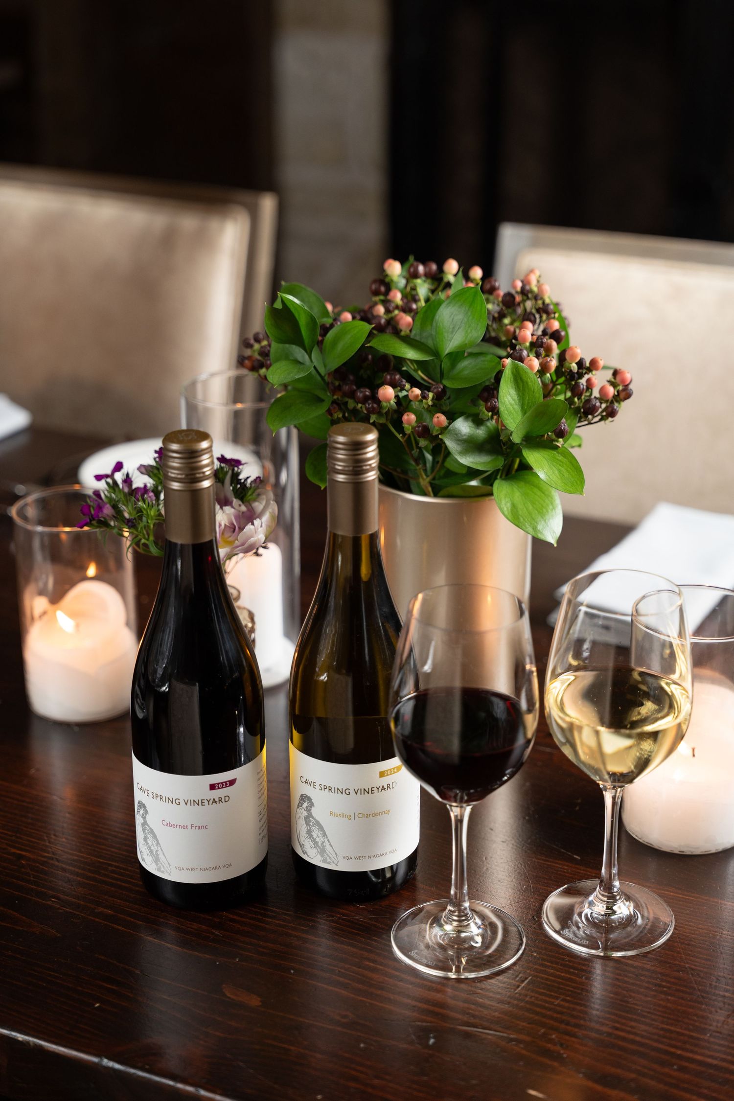 Two Loveblock Vineyard wine bottles with red and white wine glasses on a dark wood table with candles and flowers.