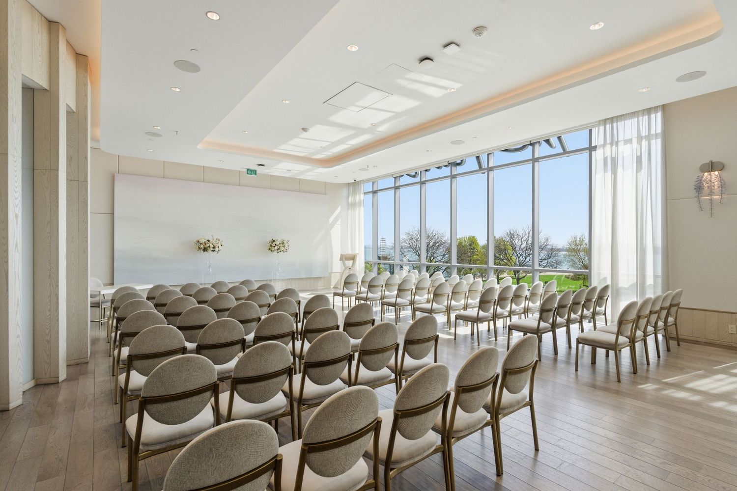 Modern conference room with rows of gray chairs and natural lighting from large windows overlooking city views.