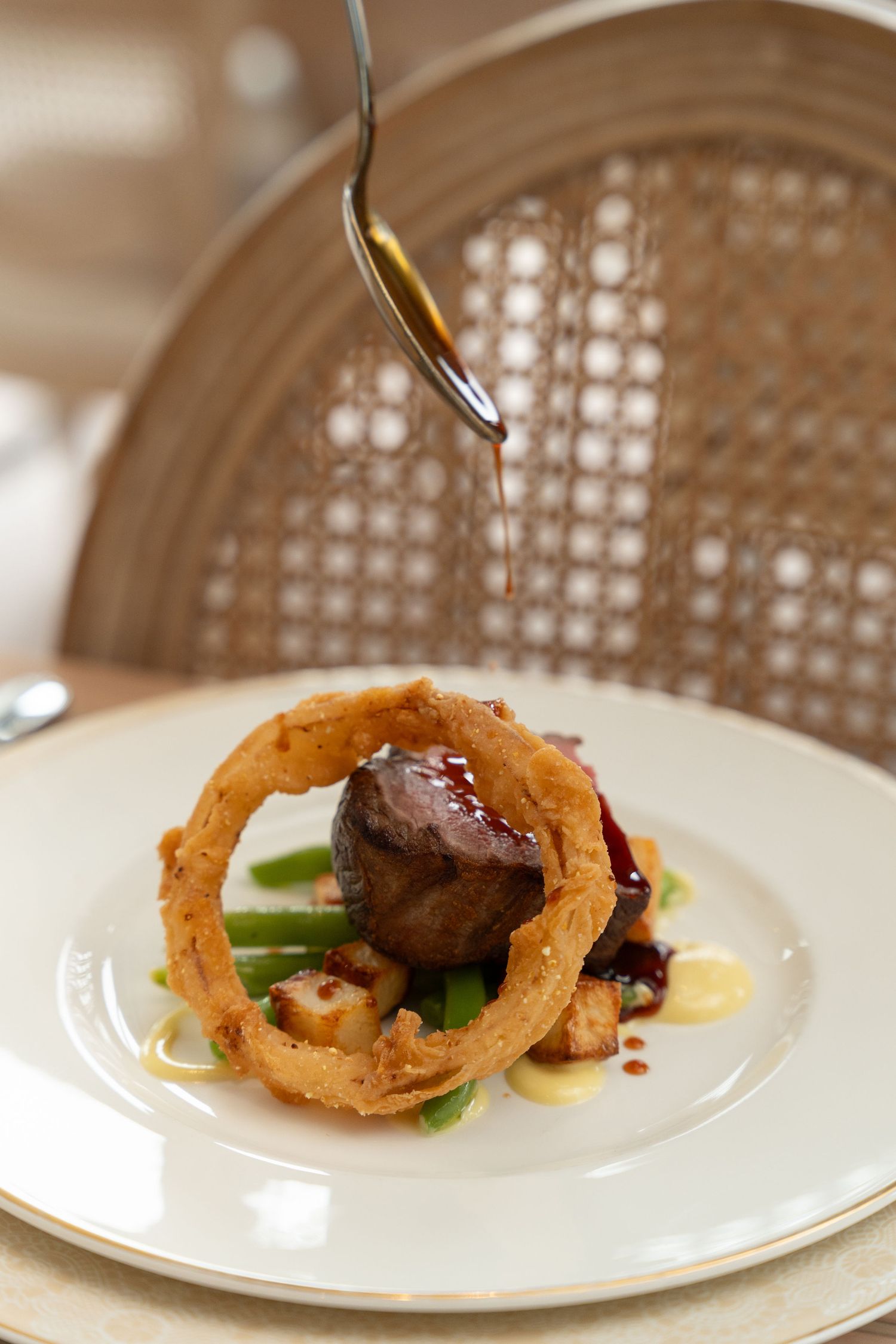 Plated dish featuring crispy onion rings and meat on white china with elegant presentation.