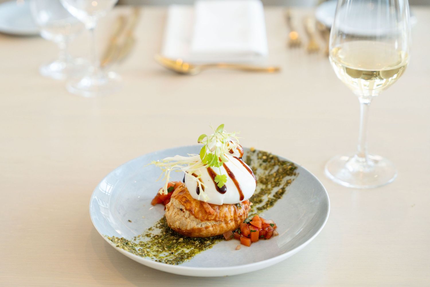 Elegant plated seafood dish with asparagus and sauce on a light blue plate with gold cutlery on white tablecloth.
