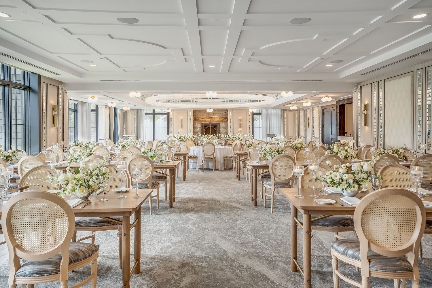 Elegant banquet hall with cream-colored decor features round dining tables, ornate chairs, and floral centerpieces.