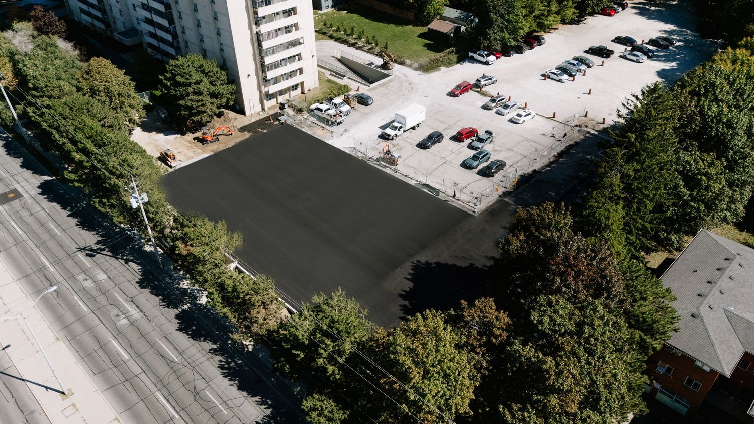 Aerial view of apartment buildings and parking lots surrounded by green trees in an urban residential area.