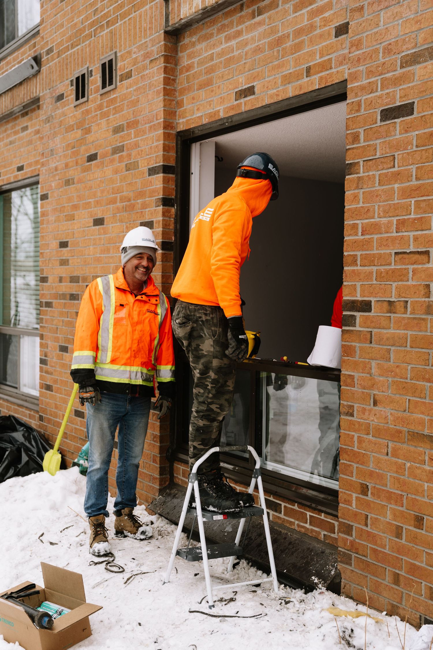 Workers installing new windows on brick building exterior during winter conditions.