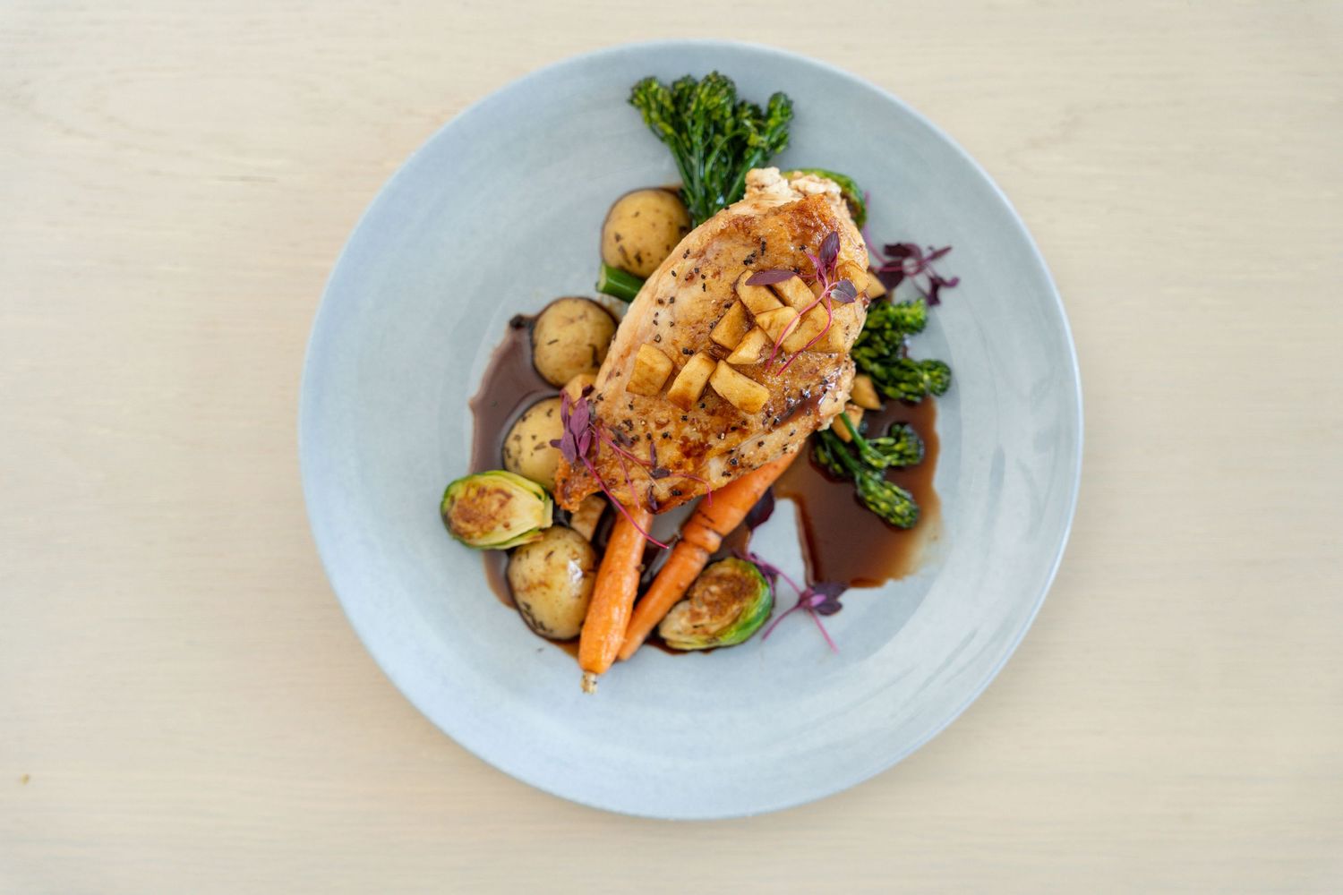 Elegant plated dishes on white plates featuring roasted meats and vegetables in an upscale restaurant setting.