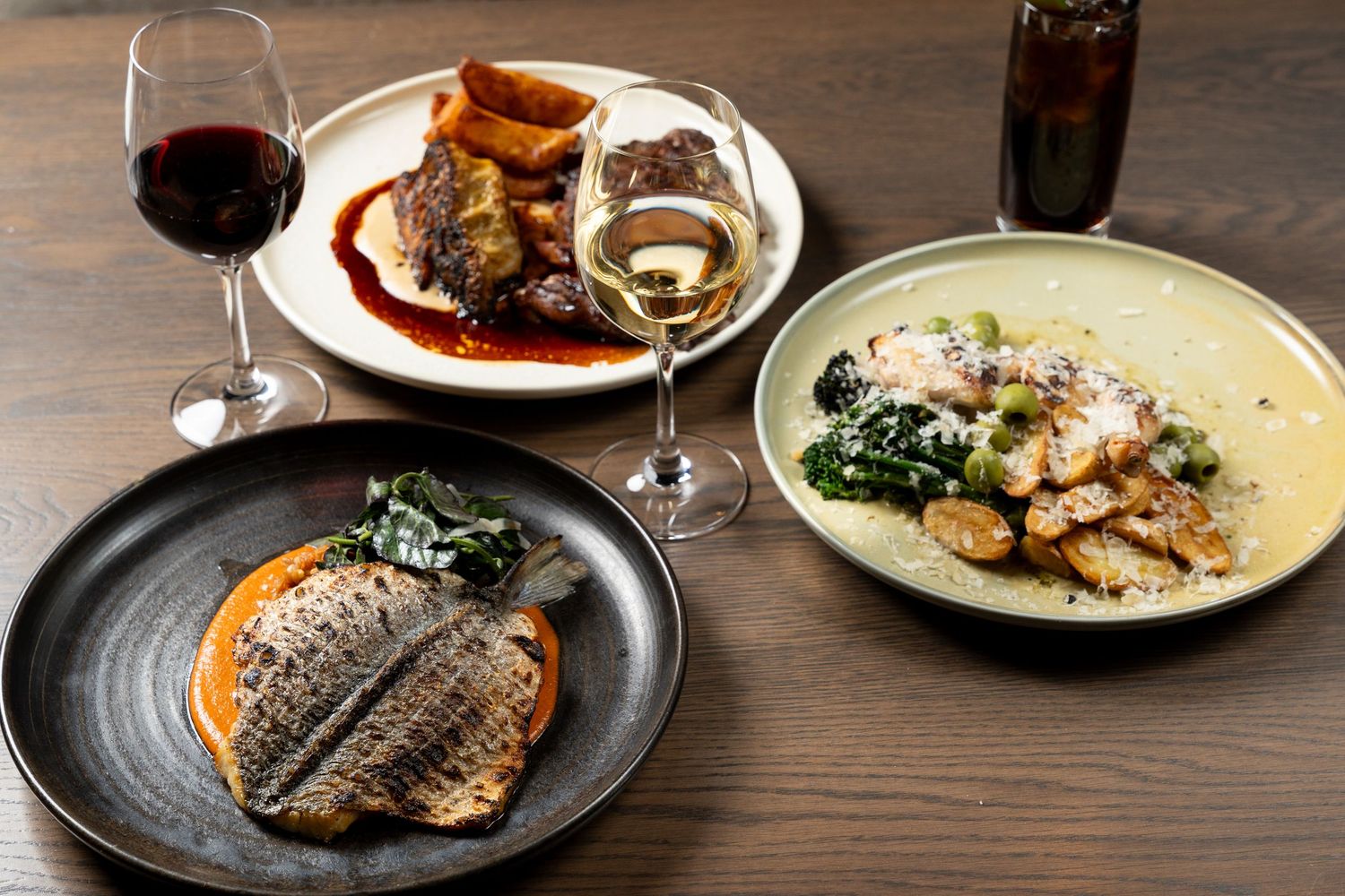 Three elegant restaurant dishes with grilled fish, braised meat, and sautéed chicken, served alongside red and white wine.