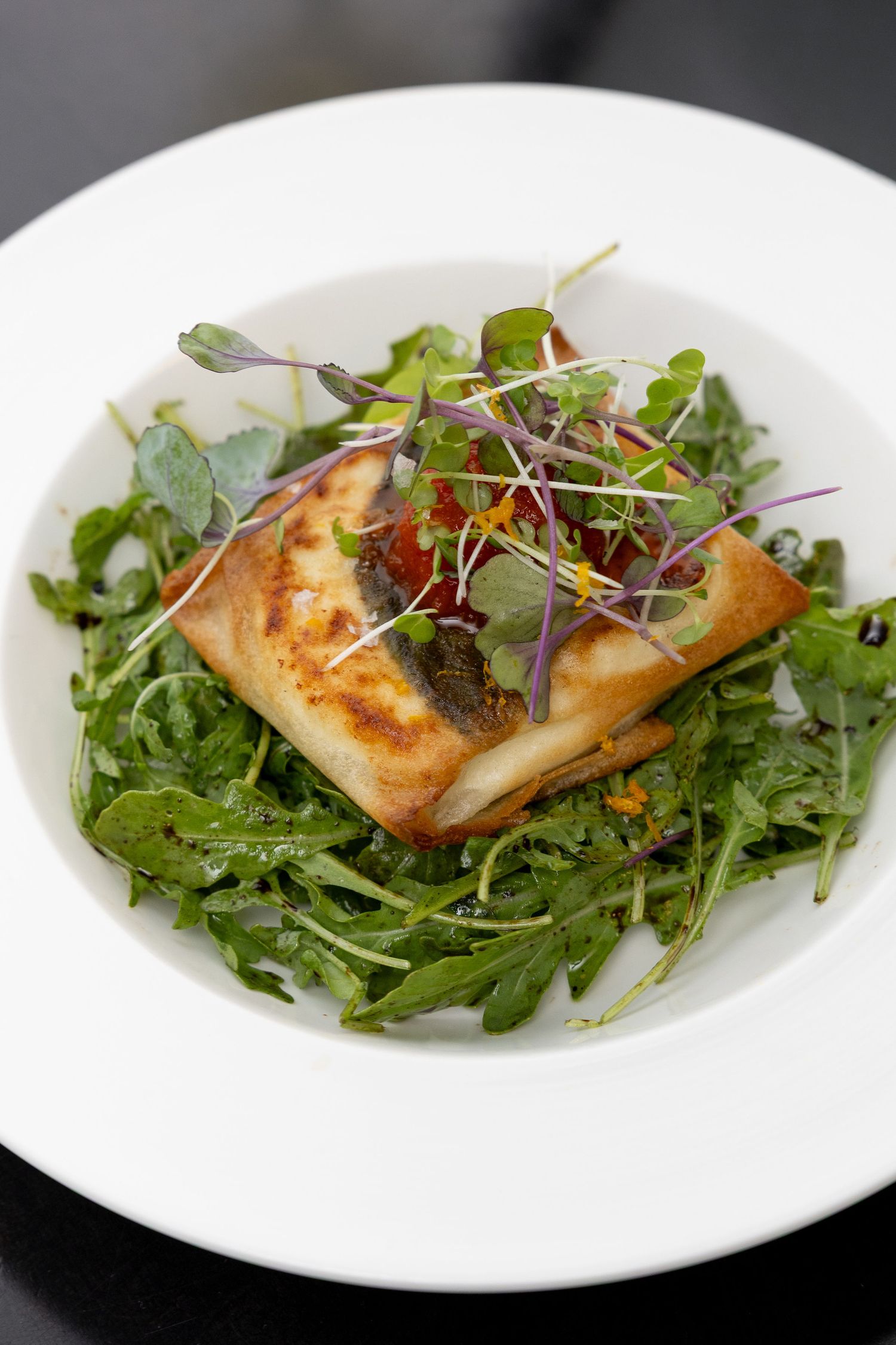 Pan-seared fish fillet served on a bed of fresh arugula and microgreens on a white plate.