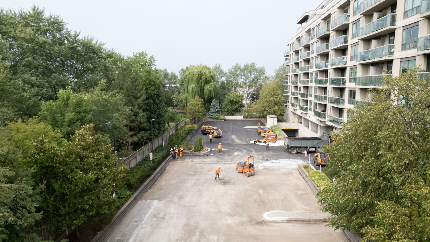 Construction workers and equipment working on a concrete surface near a modern apartment building.