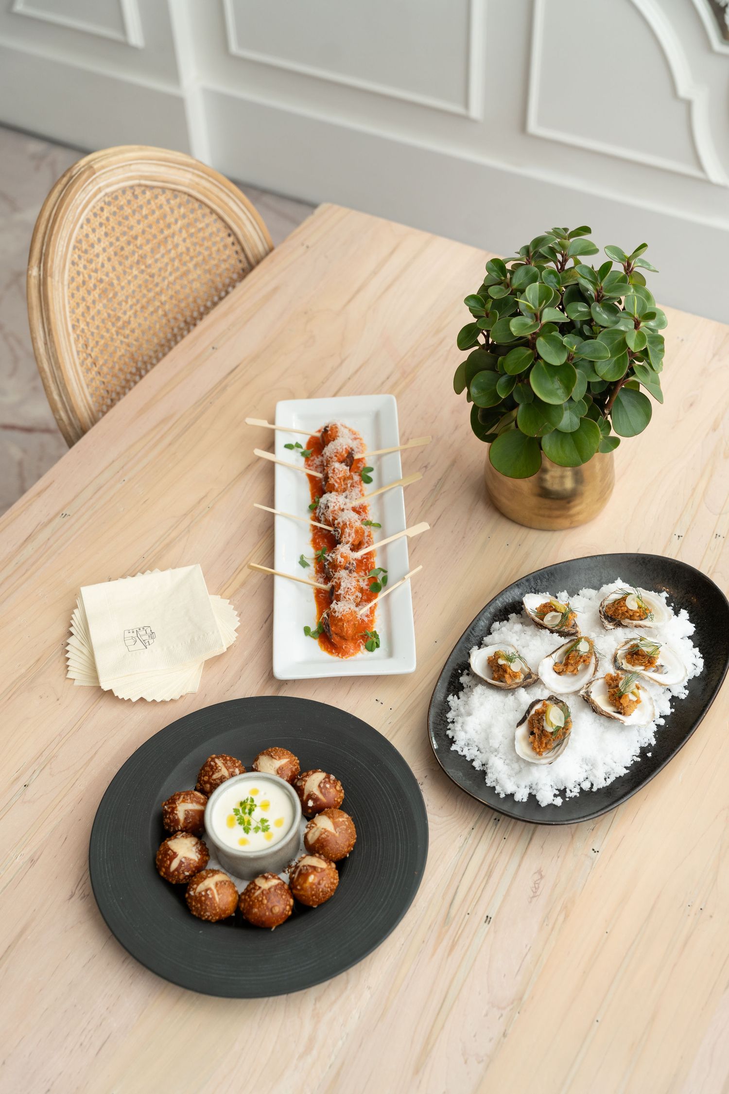 Various appetizers and small plates arranged on wooden table with decorative plant.