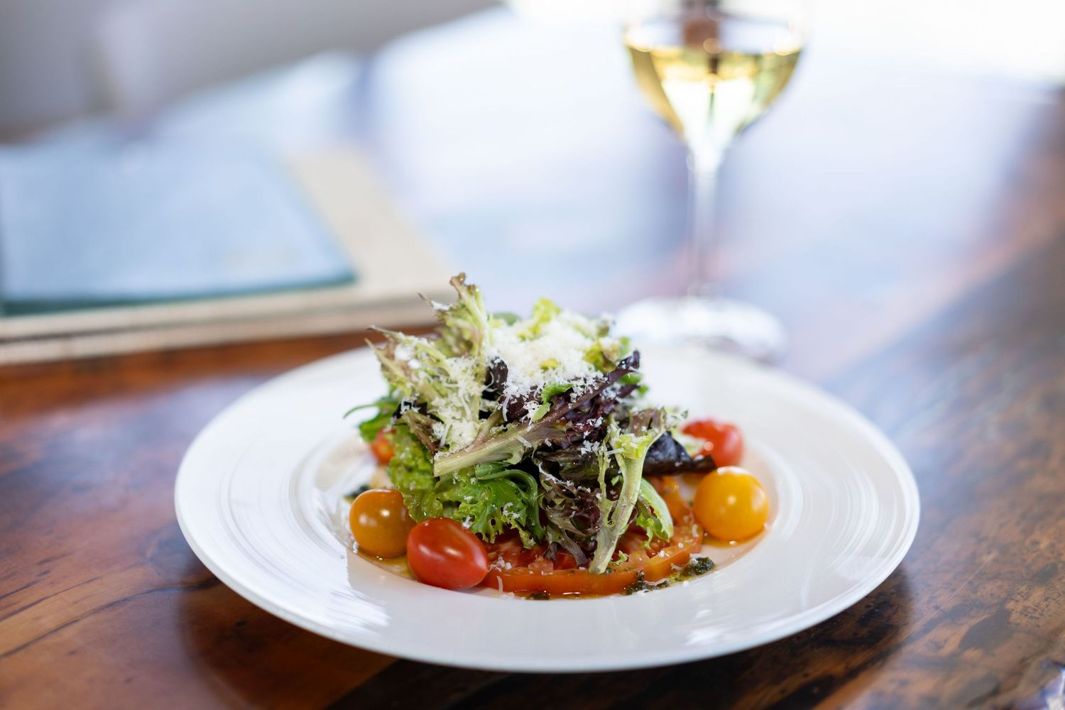Elegant plated dishes with fresh greens and colorful garnishes served on white plates in a restaurant setting.