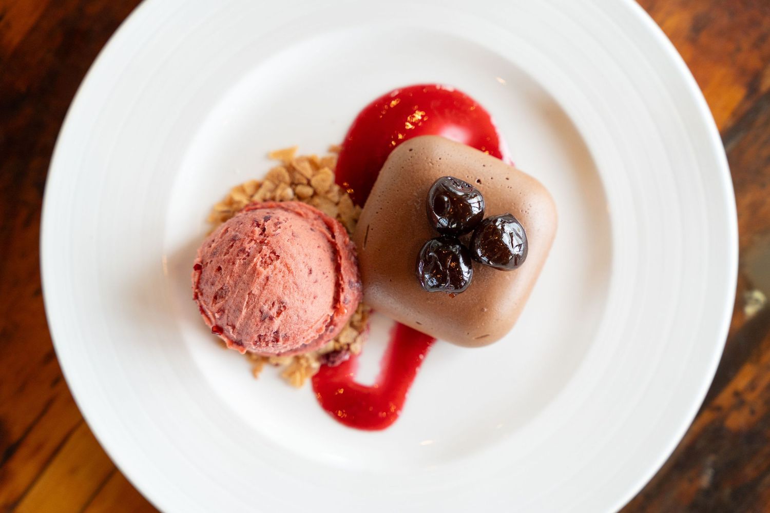 A series of white plates showcasing various plated desserts with sauces and garnishes on a wooden surface.