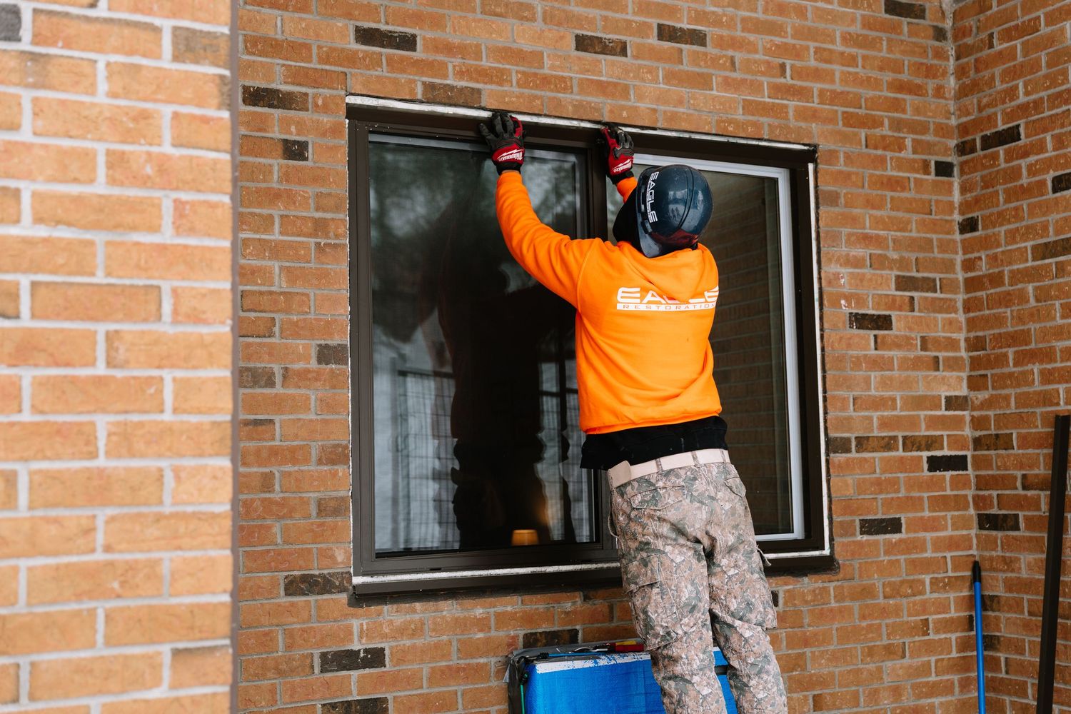 Window washers in orange safety vests clean exterior windows on a brick building using professional equipment.