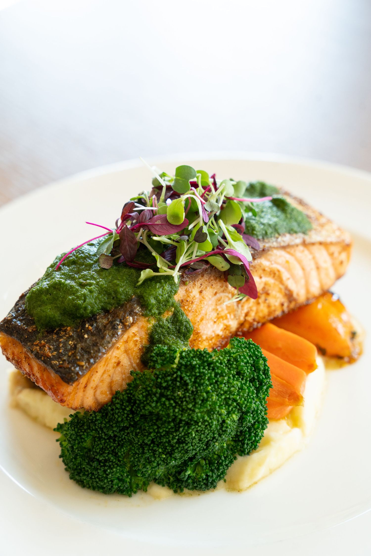 Pan-seared salmon fillet served with steamed broccoli and microgreens on a white plate.