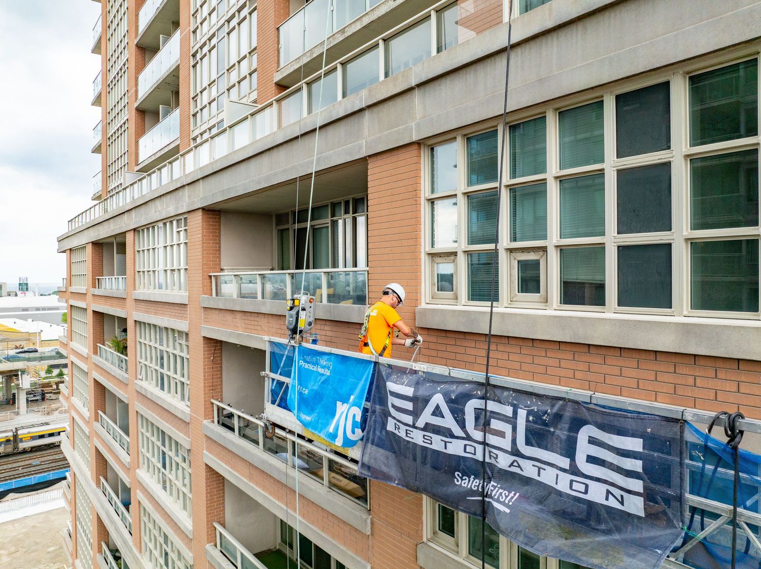 Window washer in yellow safety gear cleaning exterior windows on suspended platform of high-rise building.